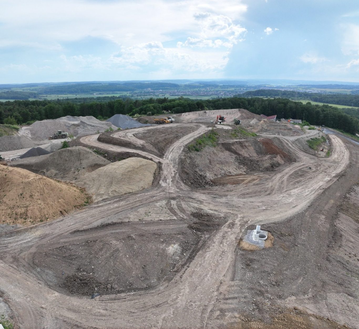 Baugelände mit unbefestigten Wegen und Aushub in einer hügeligen Landschaft.