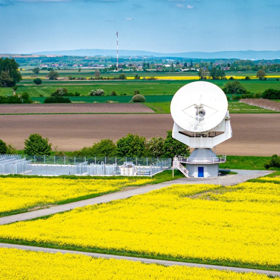 Gelbes Rapsfeld mit Satellitenschüssel und grüner Landschaft im Hintergrund.
